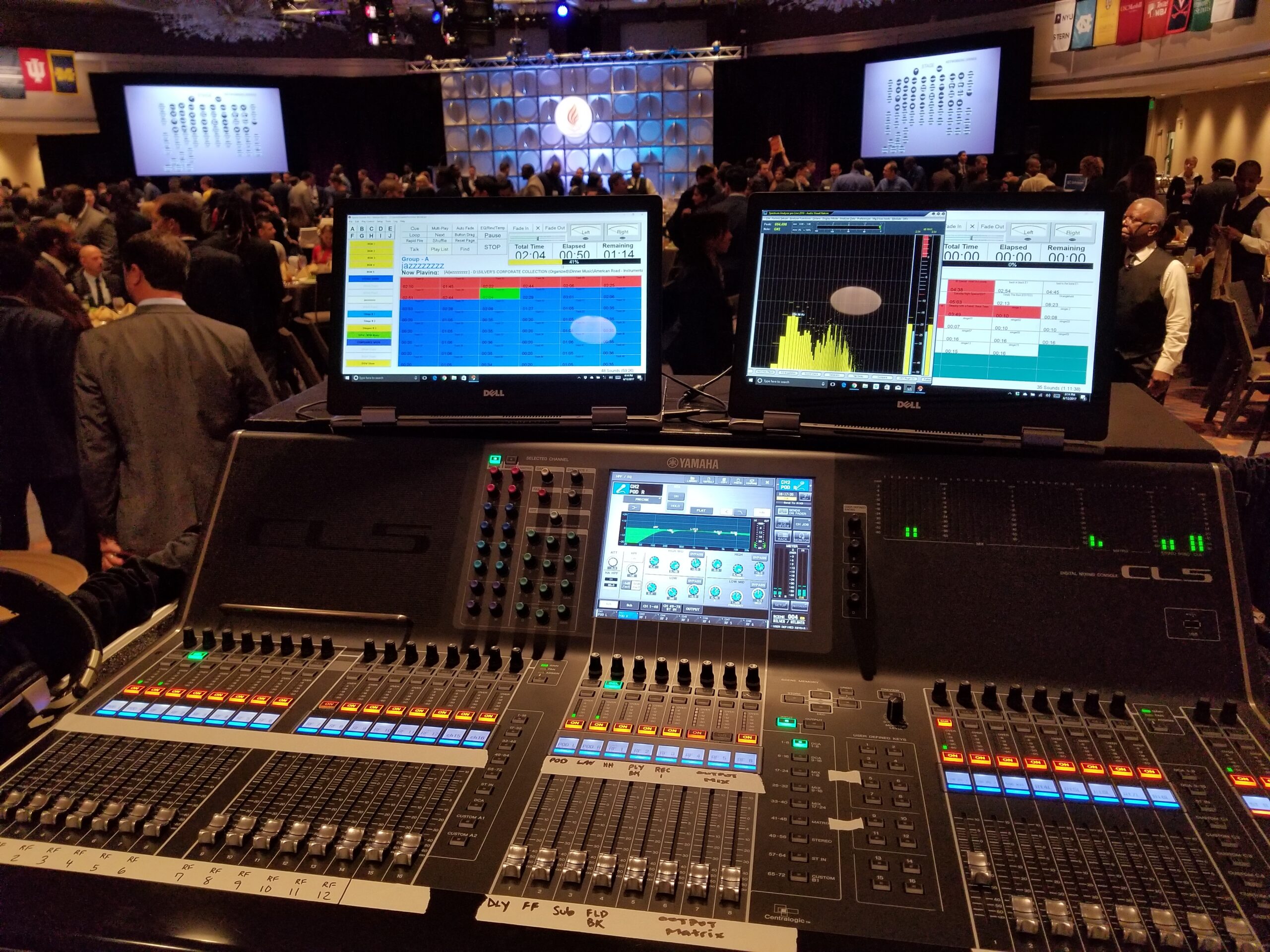 A close-up view of a sound mixing console with multiple displays, buttons, and sliders, at a live event.