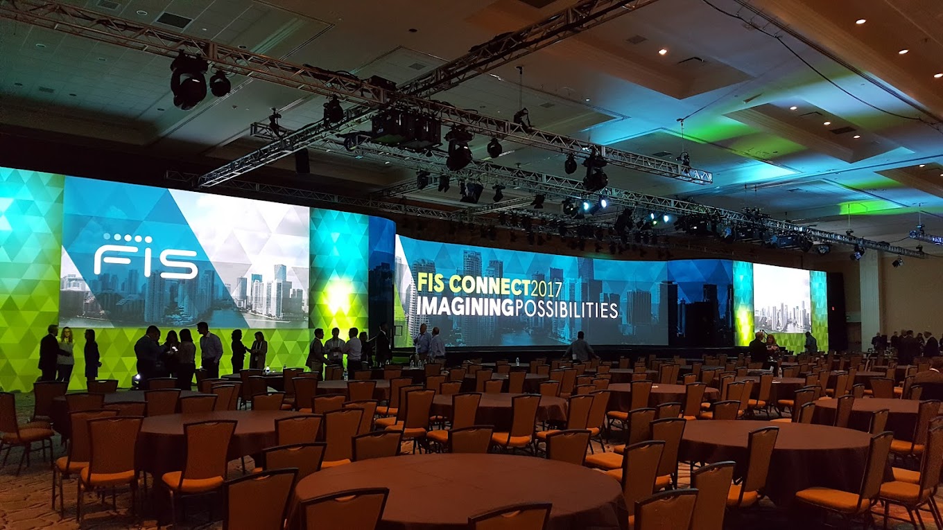 A corporate event conference room with empty chairs and a large, illuminated screen displaying "FIS CONNECT2017 - IMAGINING POSSIBILITIES" and cityscape graphics.
