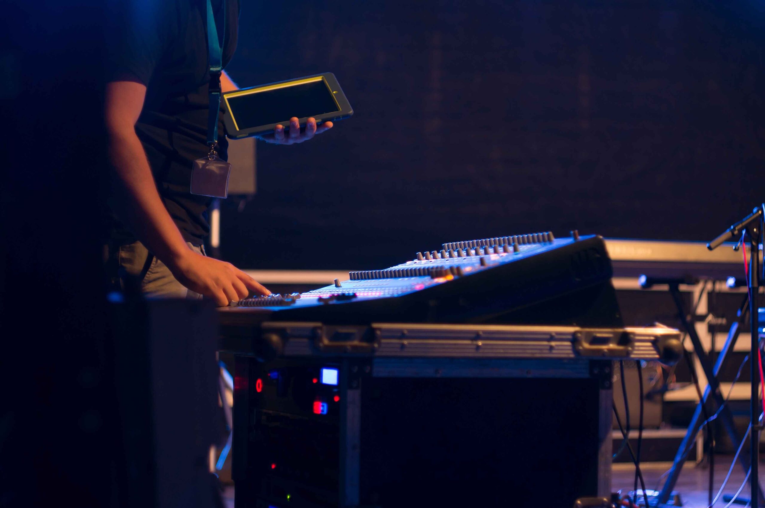 AV tech operating a sound mixing console with a tablet in hand, adjusting settings during a live event.