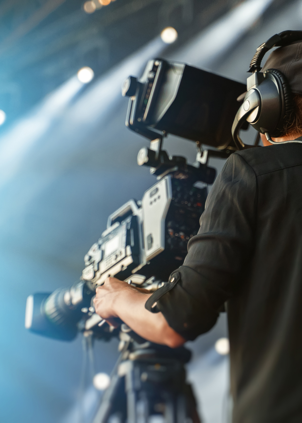 A close up image of a camera operator operating a large camera and wearing headphones.