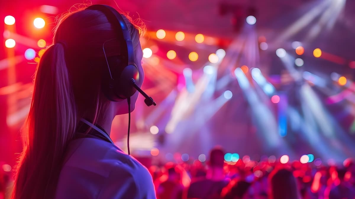 Behind-the-scenes view of an event production specialist wearing a headset, overseeing a vibrant live performance with colorful stage lighting and a captivated audience.