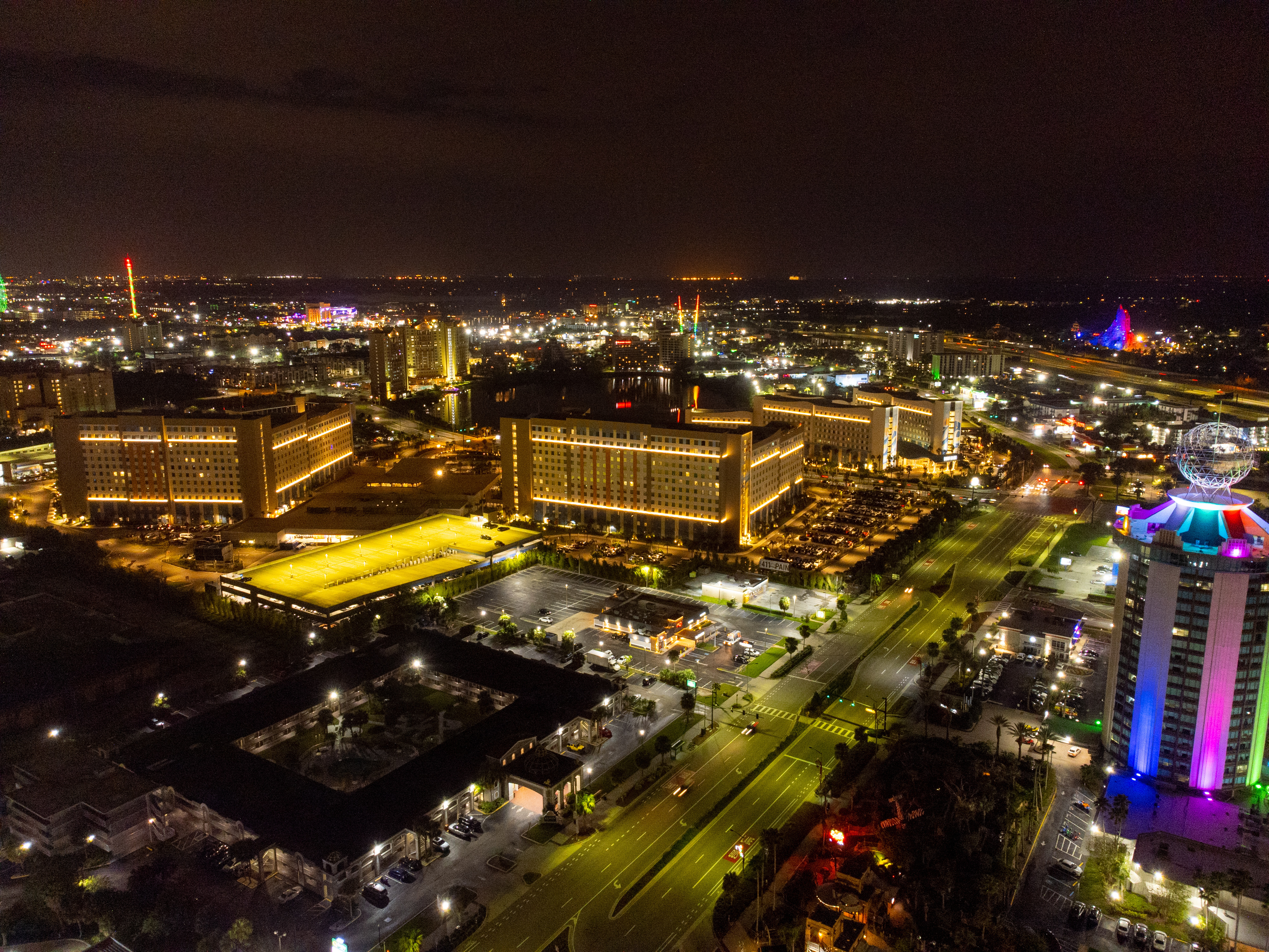 Aerial view of Kissimmee, Florida, at night. The city is illuminated with bright lights, showcasing tall buildings, streets, and colorful attractions.