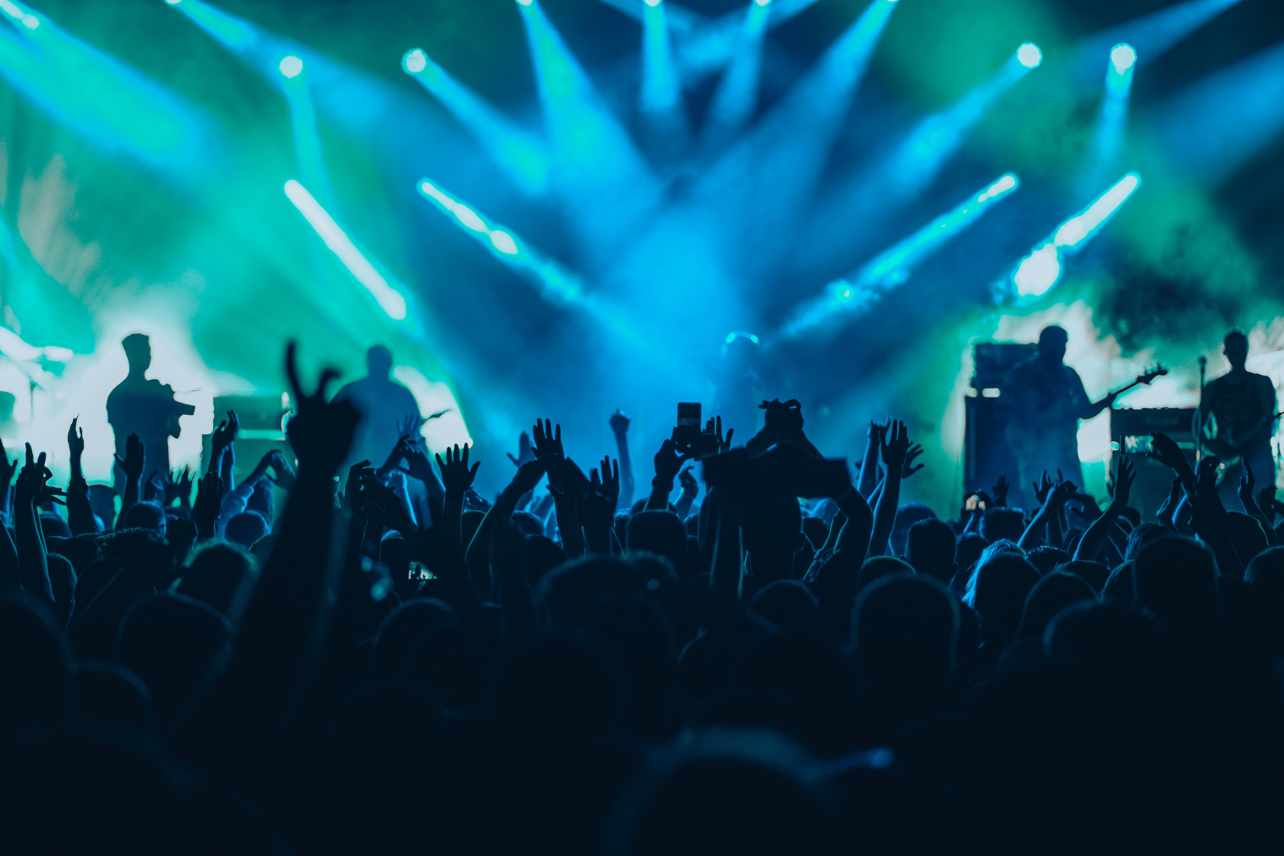 Silhouettes of a concert crowd with raised hands and musicians on stage, illuminated by blue stage lights.