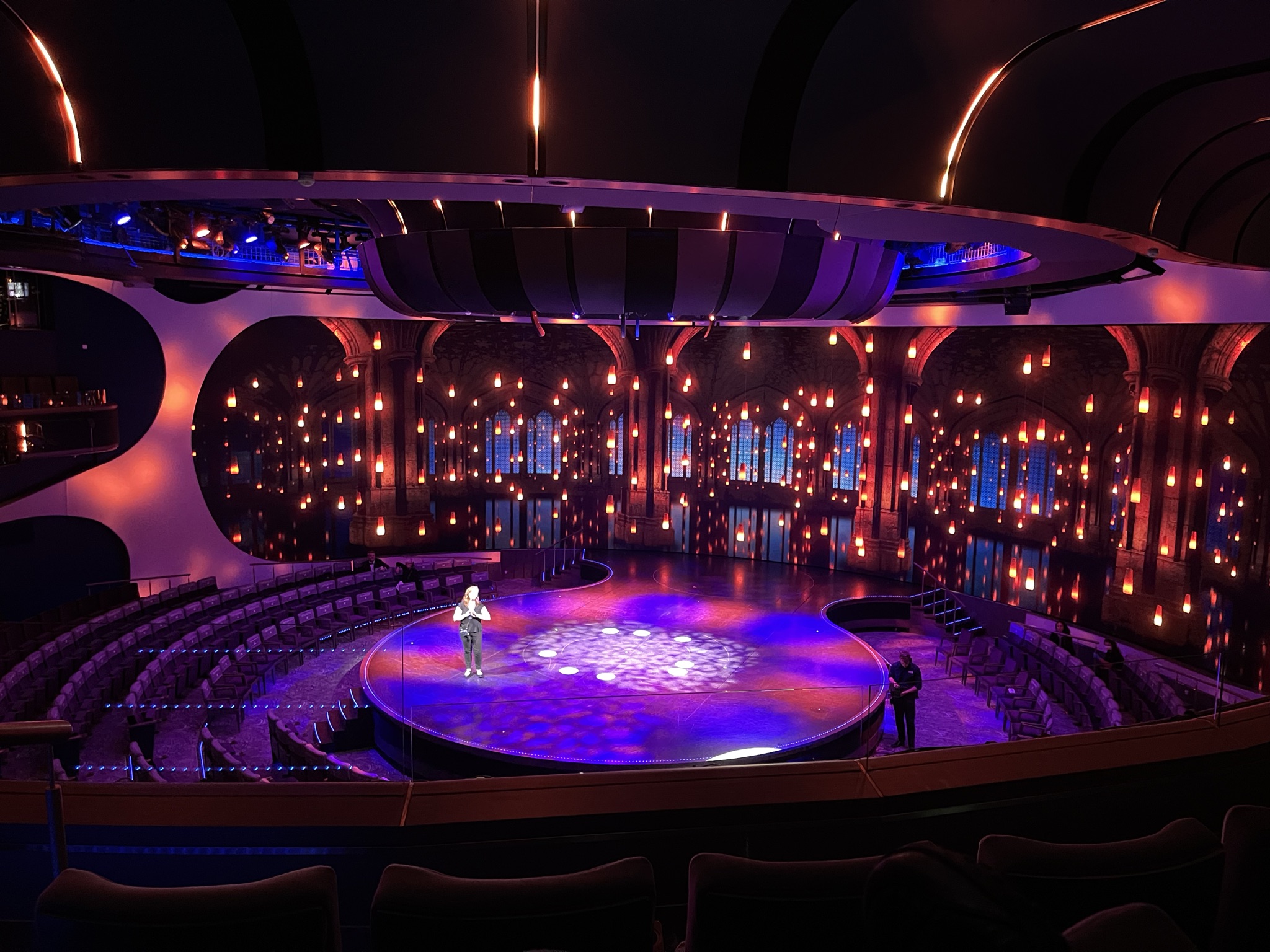 An empty theater with modern architectural features, illuminated by vibrant blue and amber lights, preparing for a performance.