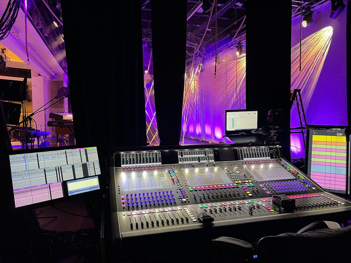 A sound mixing console with a view of a stage lit by warm stage lights, part of an event or concert setup.