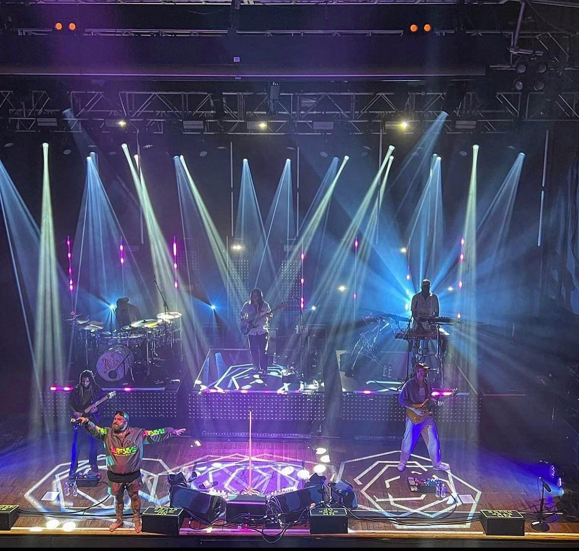 Band on stage staging in the spotlight with dynamic lighting surrounding them.