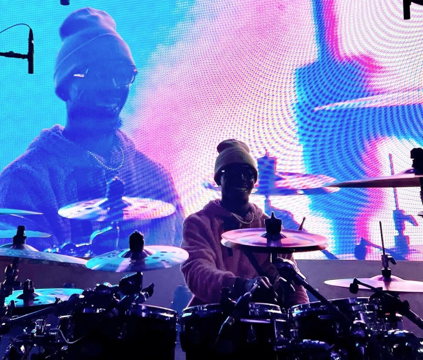 A drummer on stage performing, with a vibrant backdrop LED screen displaying an enlarged image of him in the background.