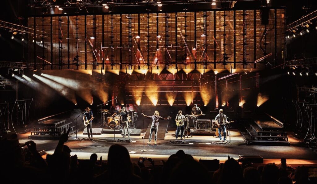 A band performing on stage with dramatic lighting and a captivated audience in the foreground.