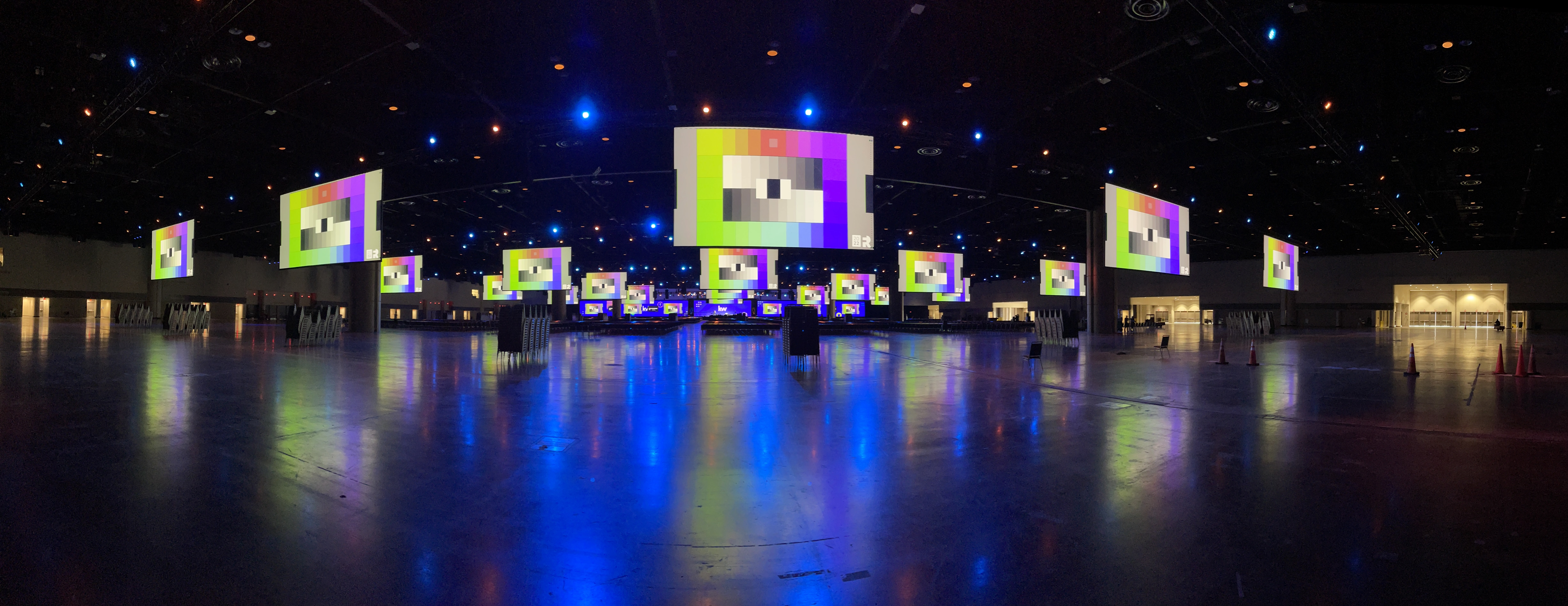 Wide-angle view of a large convention center with multiple large video screens displaying colorful graphics.