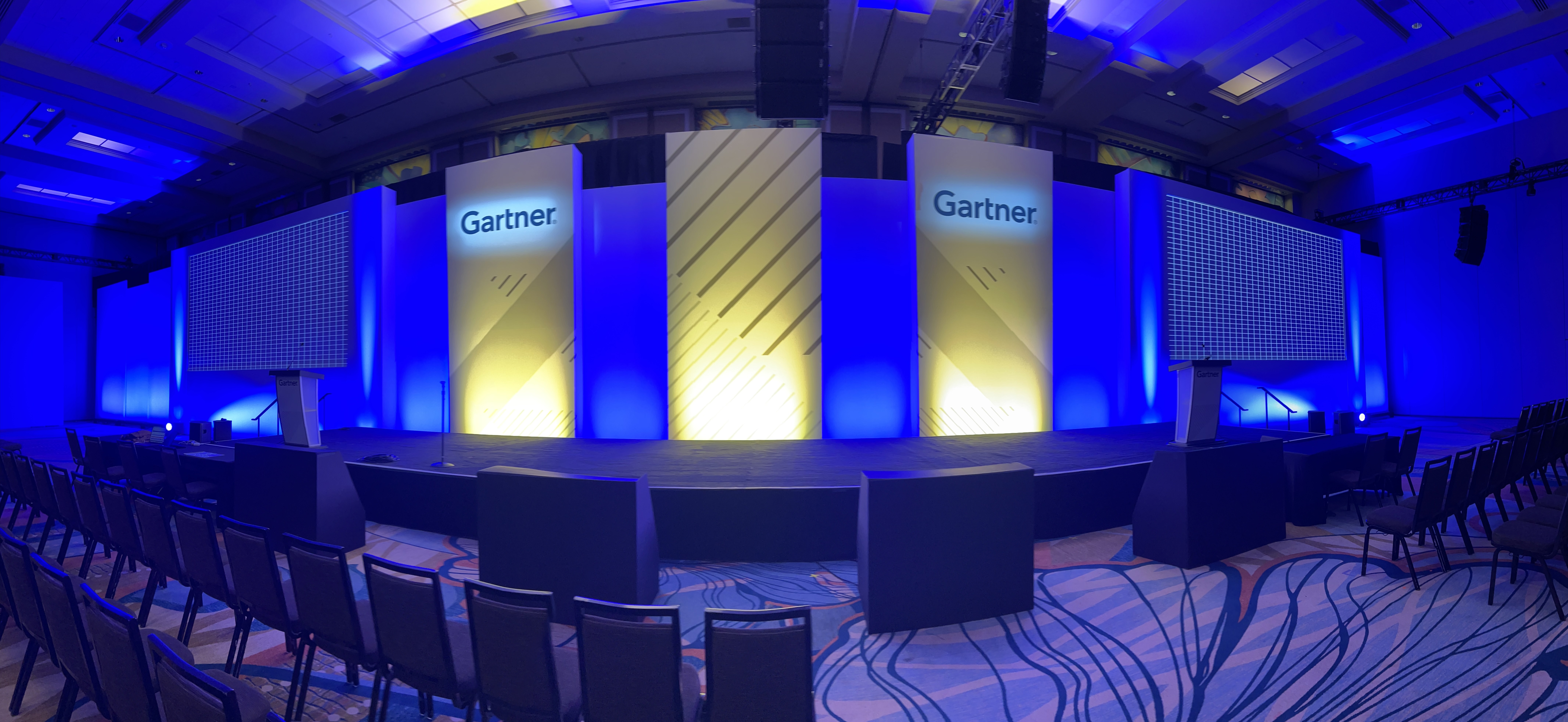 A wide view of an empty conference room with "Gartner" projected on big screens.