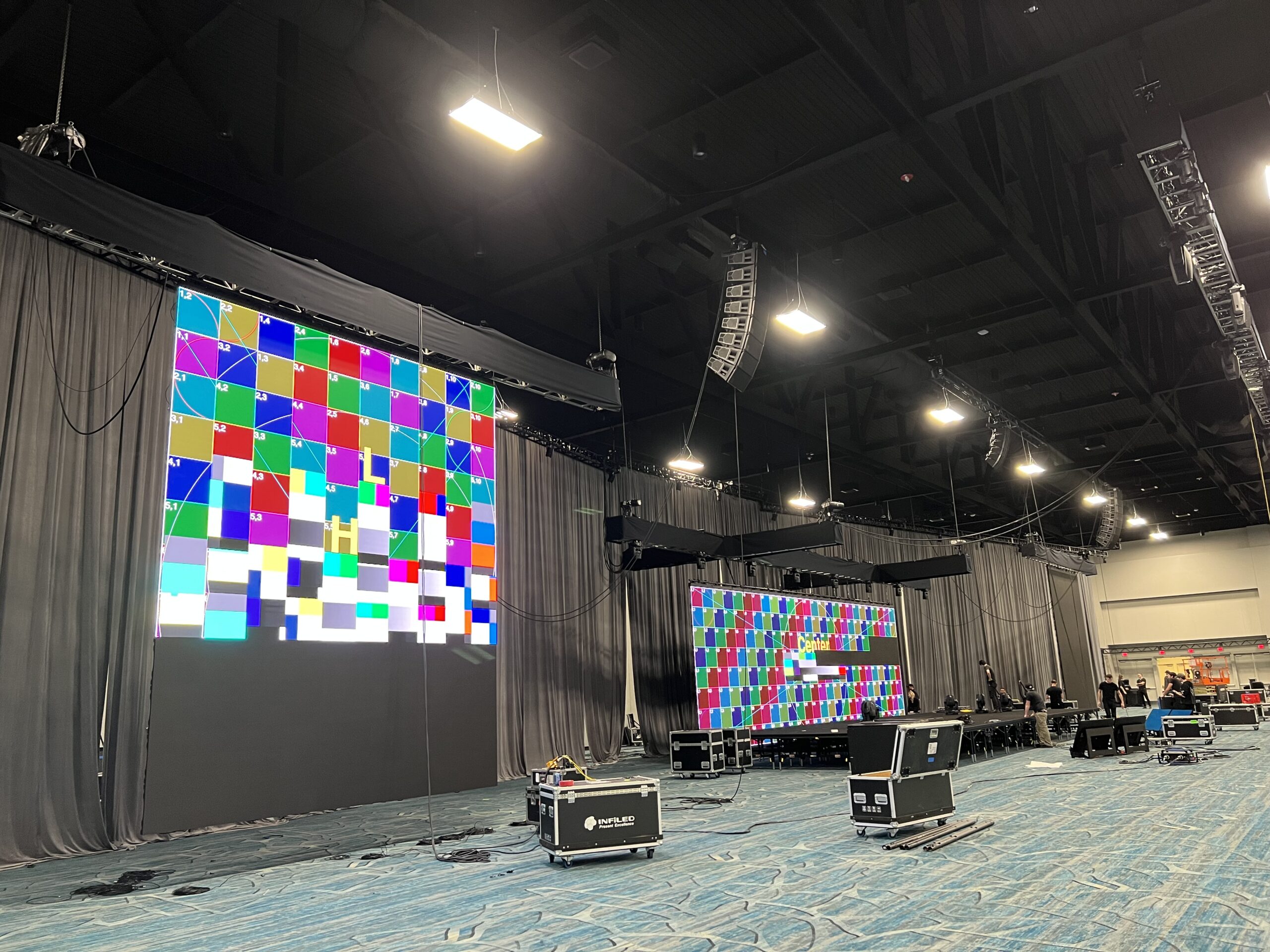 A well-lit event space with a large LED screen displaying colorful test patterns, surrounded by black curtains and event equipment.