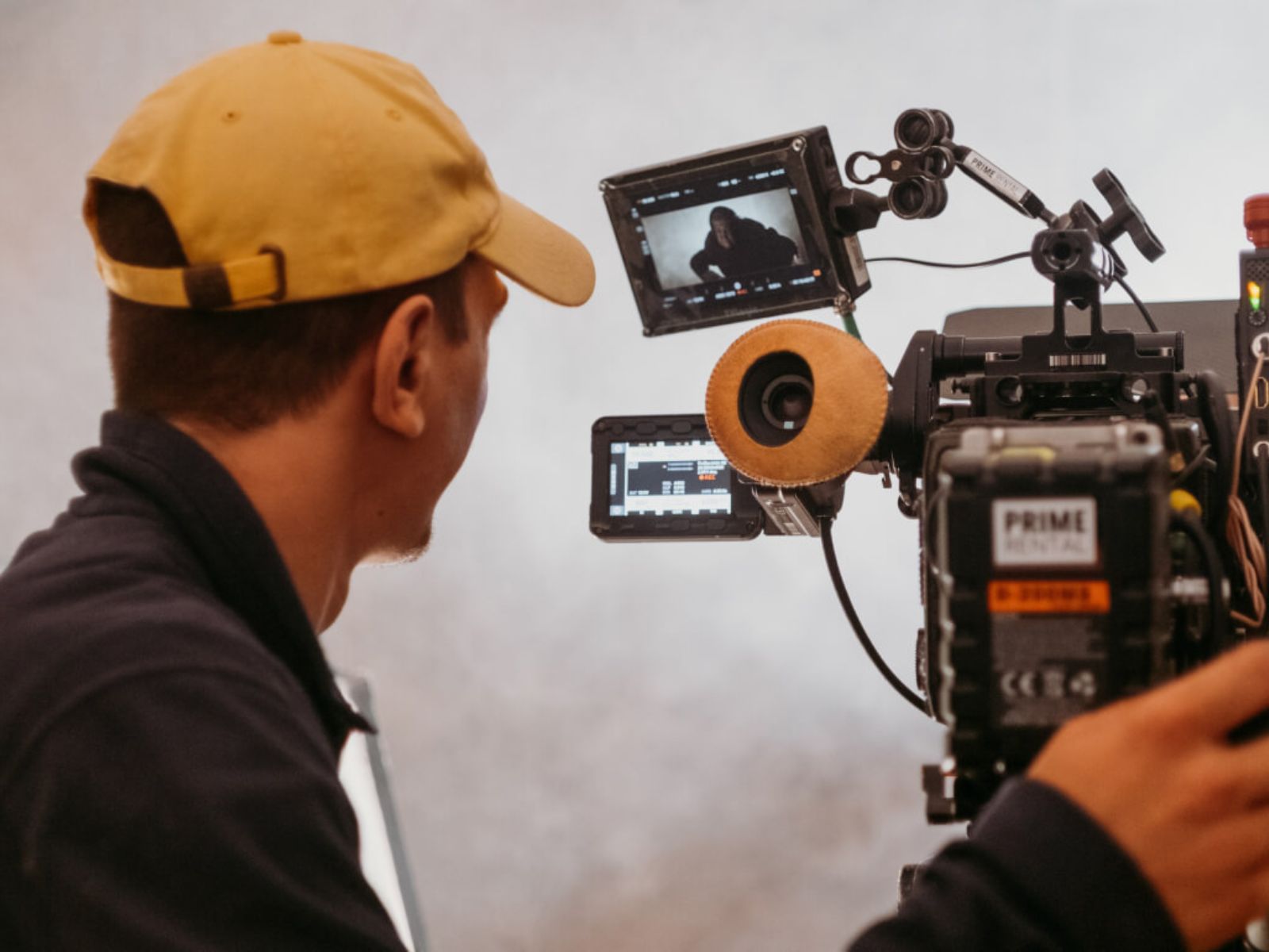 Person in a yellow cap operating a professional film camera with a monitor attached.