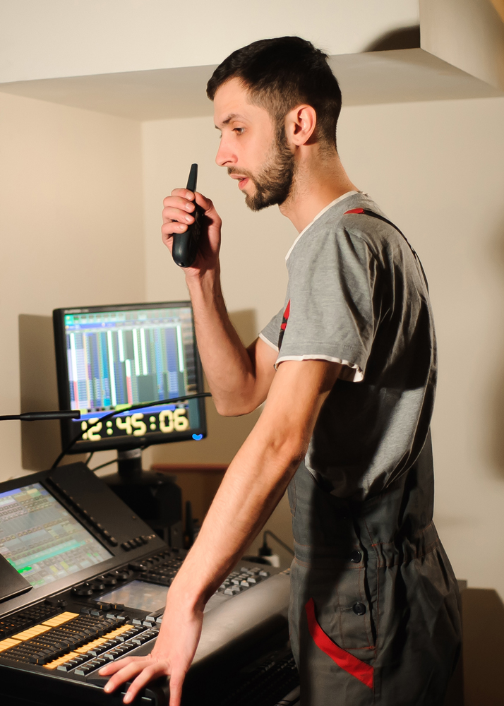 A technical director standing in front of a lighting console and holding a walkie talkie
