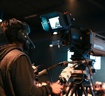 A Man in Headphones Operating a Camera on Tripod