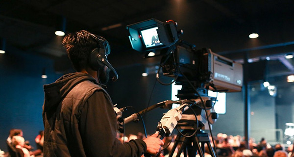 A Man in Headphones Operating a Camera on Tripod