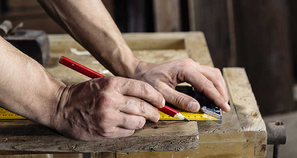 A Man Drawing With a Wooden Ruler on Wood