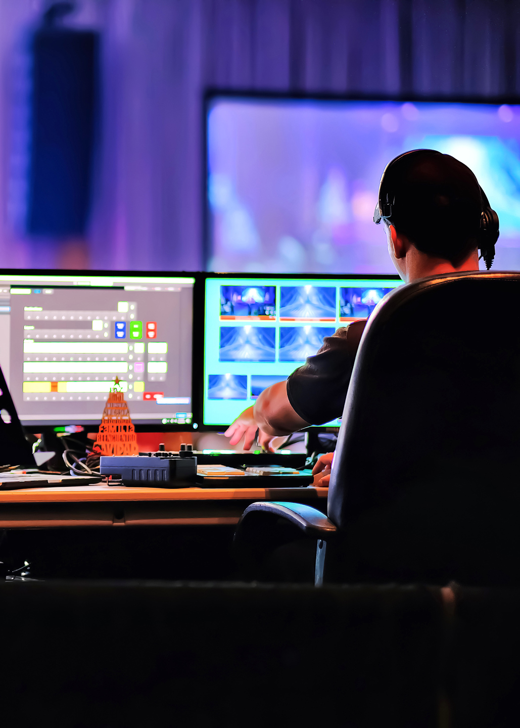 A video operator sitting in front of multiple screens in a control room, wearing headphones and interacting with an audiovisual mixing console.